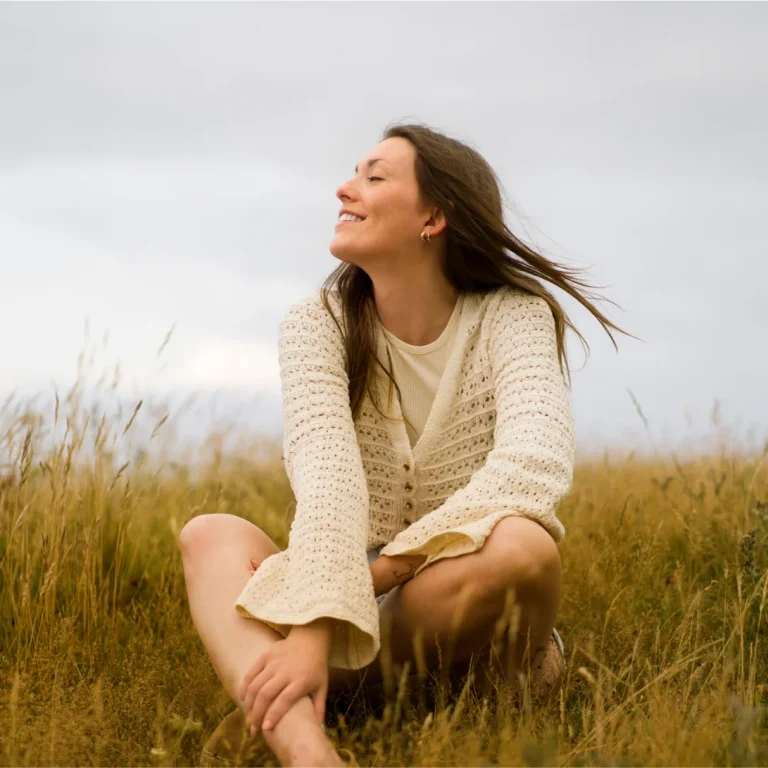 Woman sitting in a field, smiling and enjoying nature, representing themes of recovery and well-being in mobility restoration therapy.